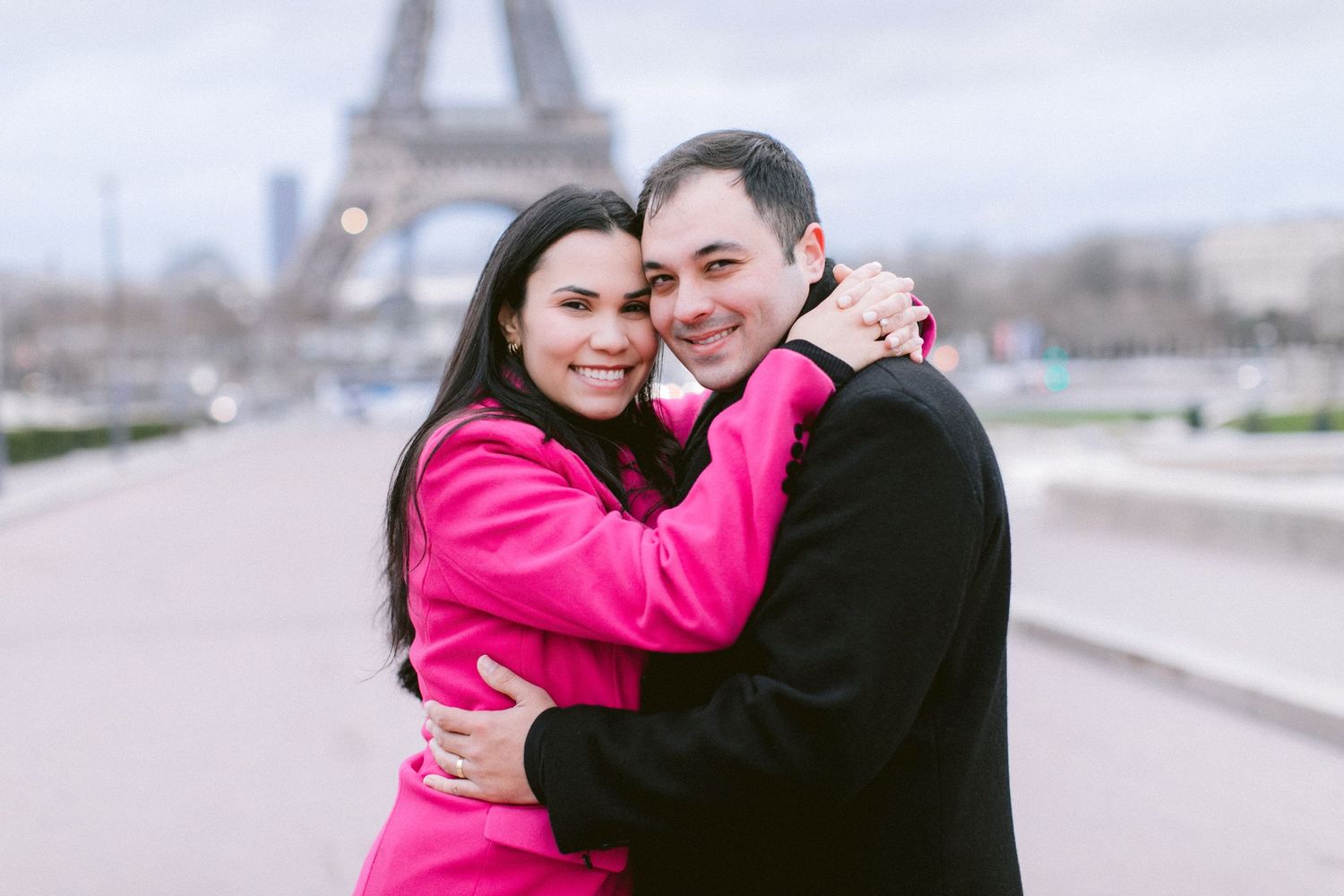 Romantic embrace with the Eiffel Tower visible in the background on a cloudy day.