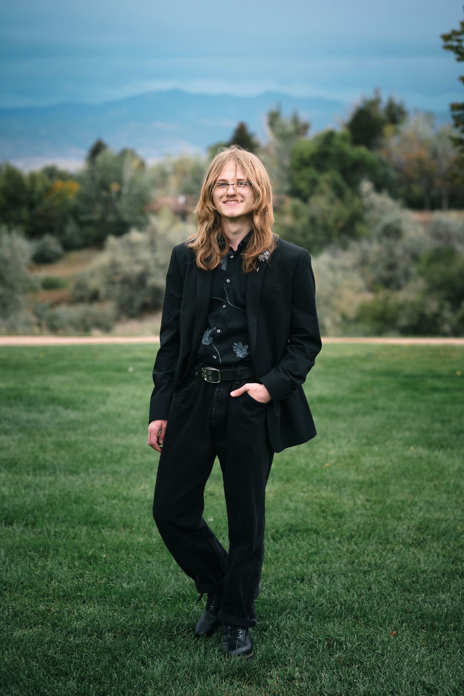 Professional portrait on green lawn wearing all black attire with mountains in distance.
