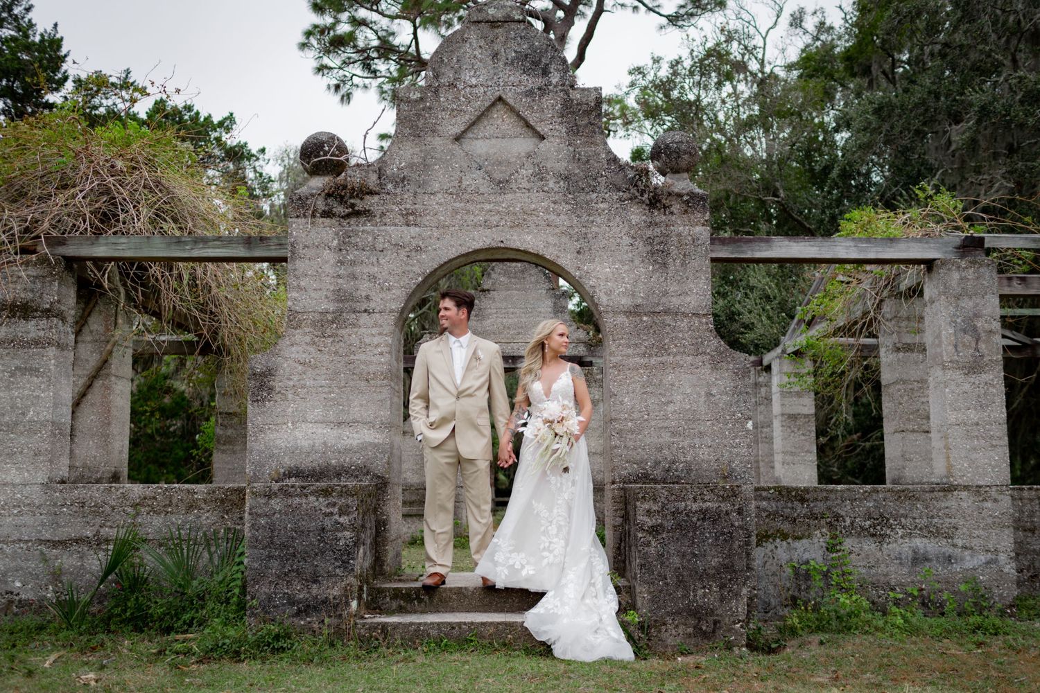Elegant couple standing in stone archway ruins during outdoor wedding photo session.