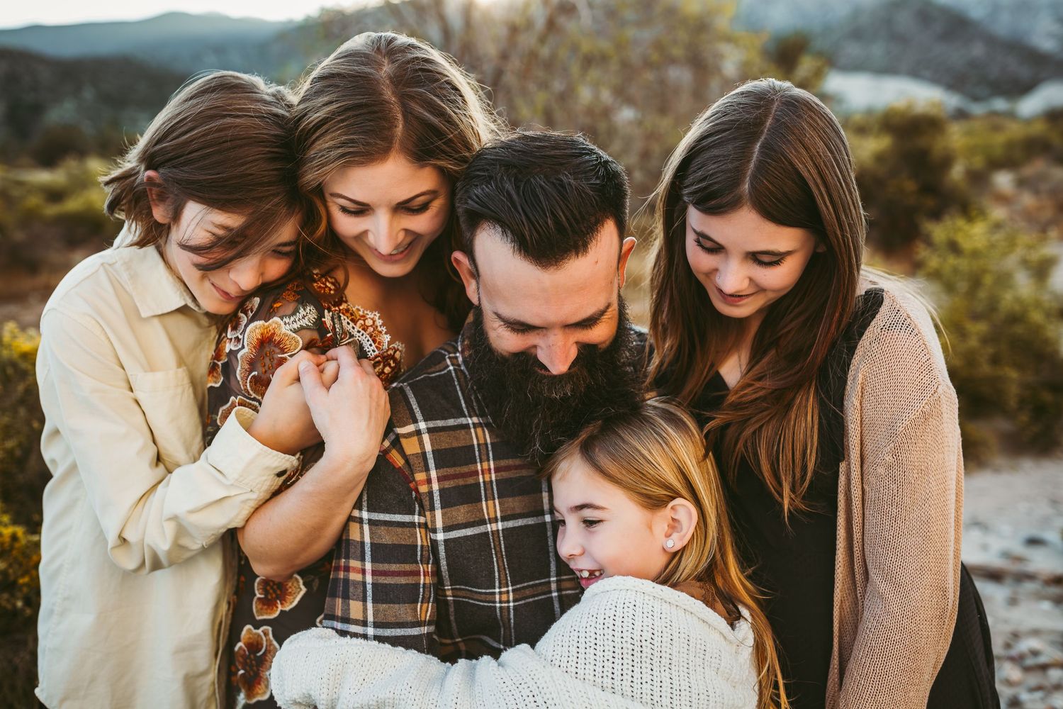 Family embracing together outdoors against a mountainous backdrop during golden hour.