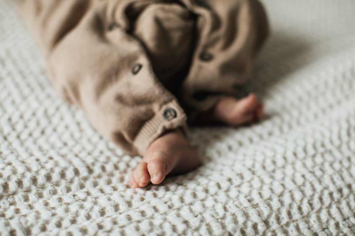 Close-up of newborn baby feet in a brown button onesie on a knit blanket.