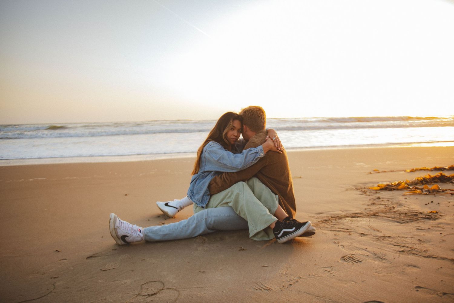 A couple shares an intimate moment while sitting on a sandy beach at sunset.