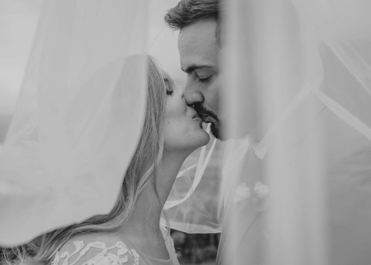 Romantic black and white portrait of a couple kissing behind a delicate wedding veil.
