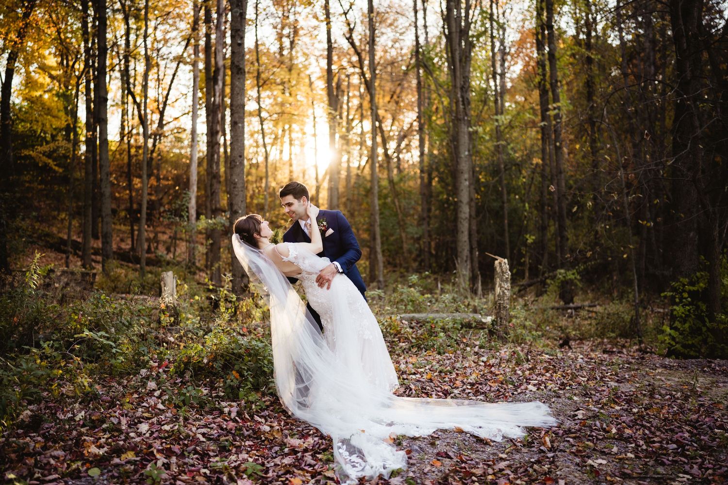 A romantic wedding portrait of a couple dancing in a wooded area with flowing white dress and golden sunlight.