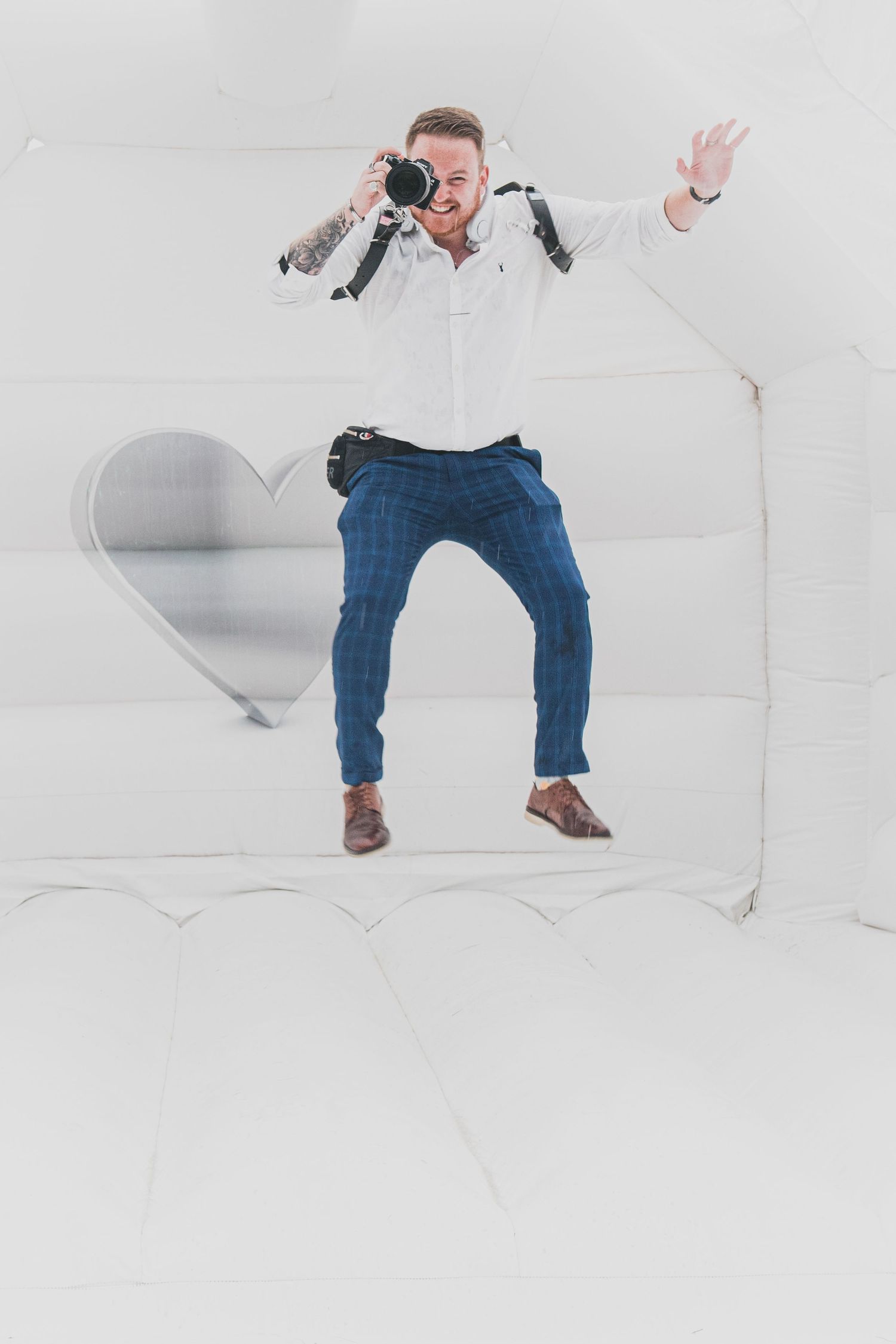 A photographer in white shirt and jeans strikes a dynamic pose against a white backdrop with a heart shape.