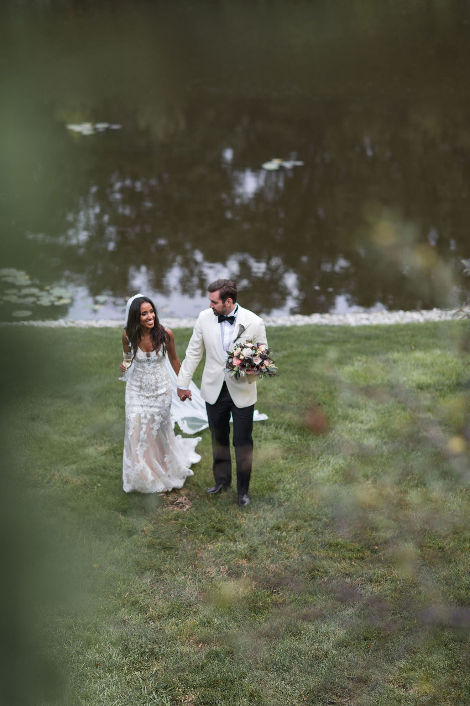 Newlyweds walking through misty garden landscape holding bouquet and each other's hands.