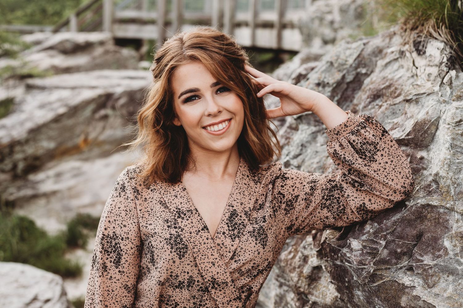 Woman in floral dress posing against textured rock wall backdrop during outdoor photoshoot.