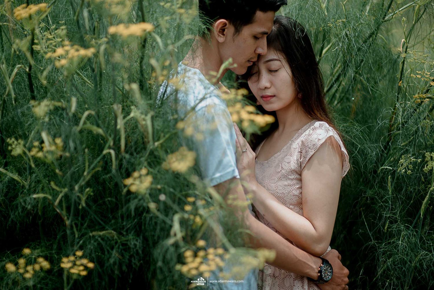 Romantic pre-wedding portrait in natural setting with tall grass and yellow wildflowers.