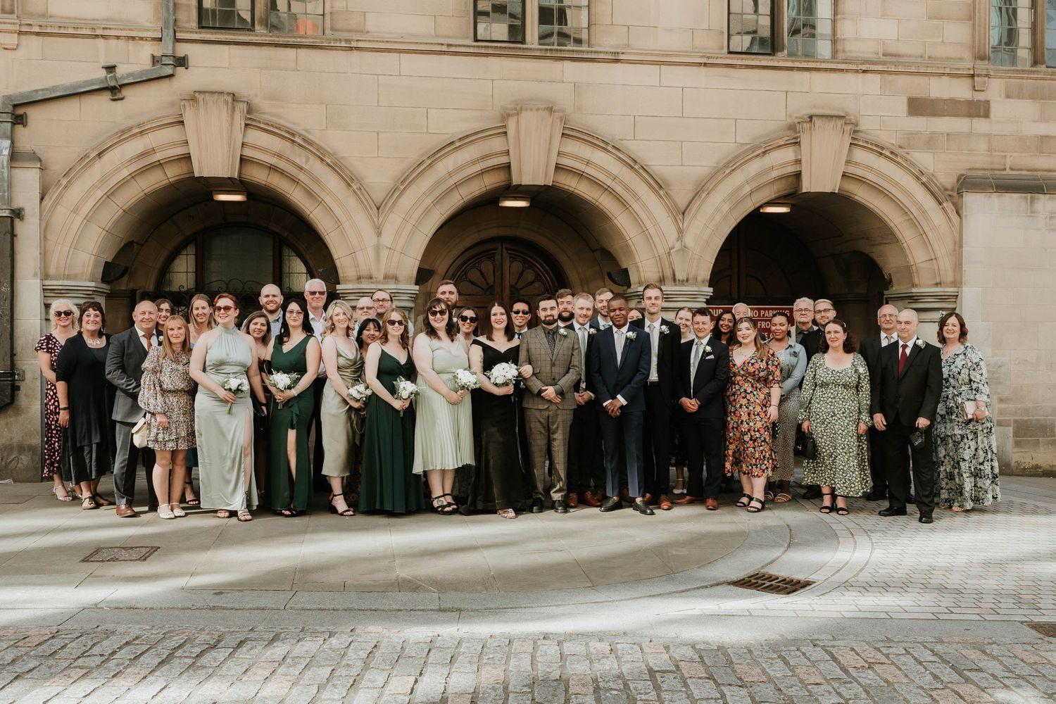 Large wedding party gathering on historic stone building steps for a formal group photo.