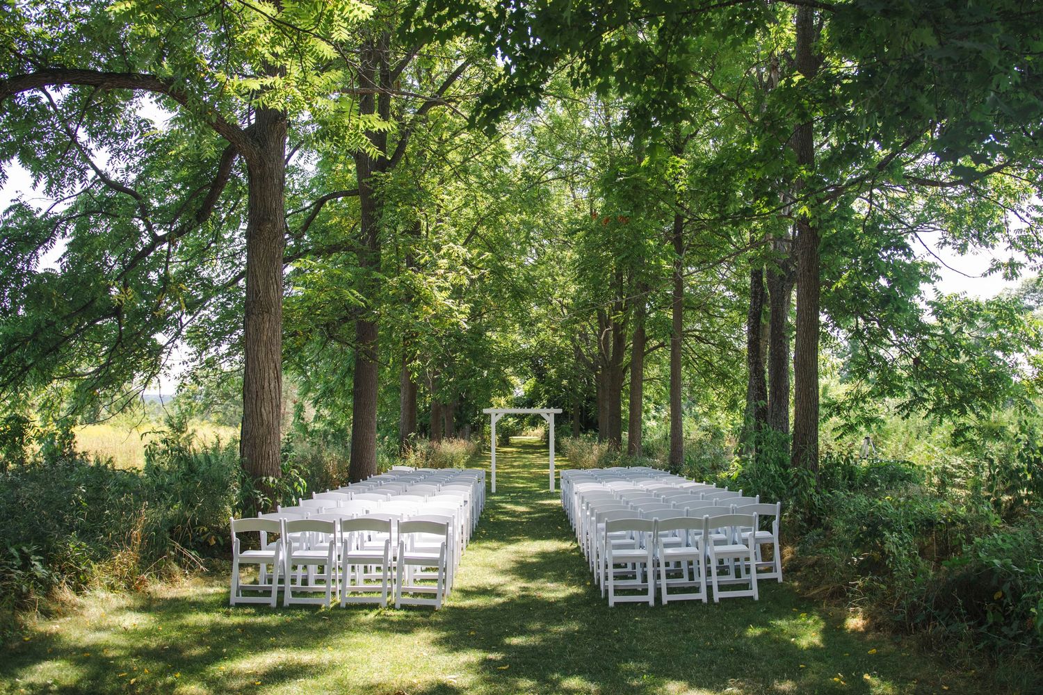 White folding chairs set up for an outdoor wedding ceremony in a serene wooded setting.