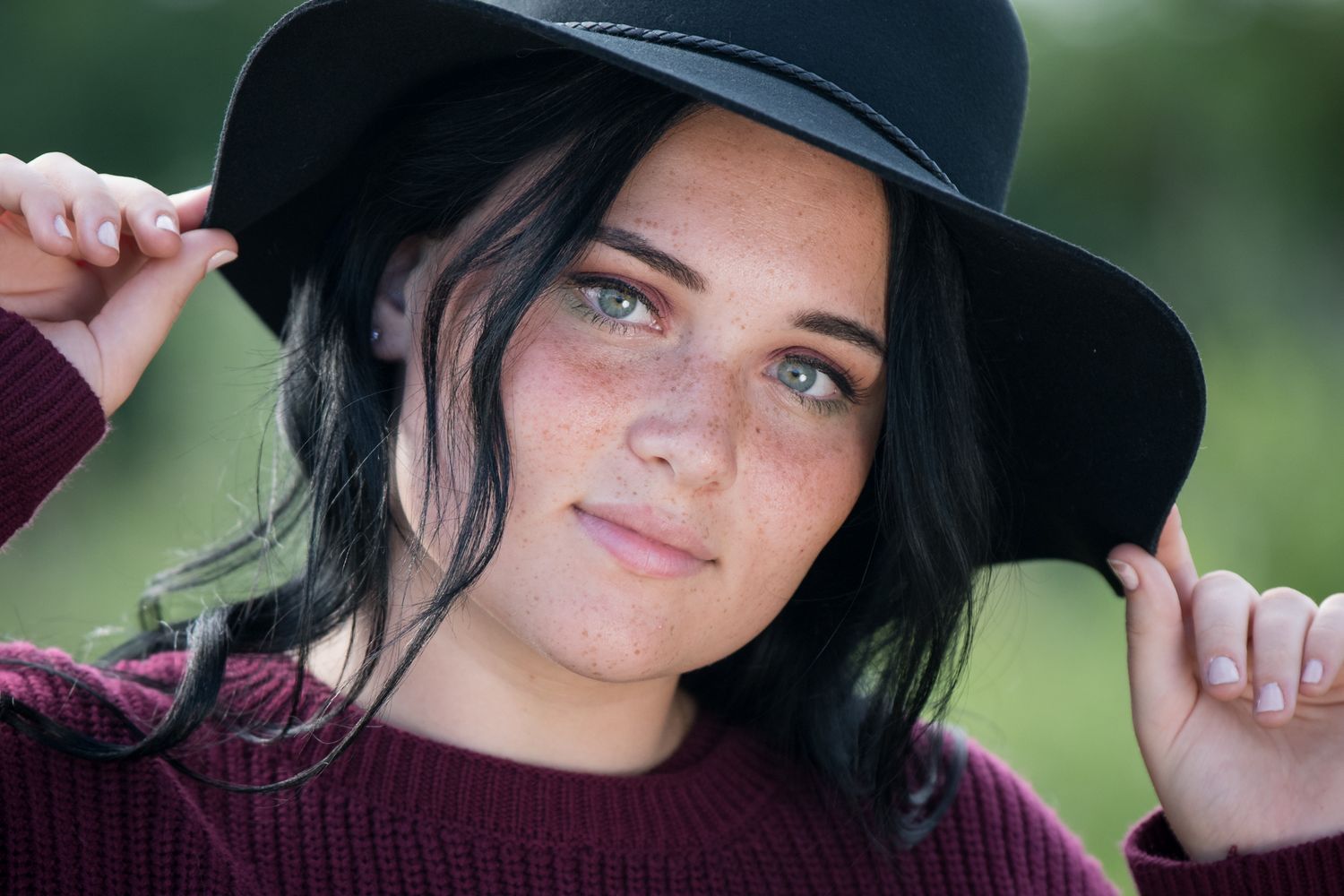 Outdoor portrait wearing a black wide-brim hat and burgundy sweater.