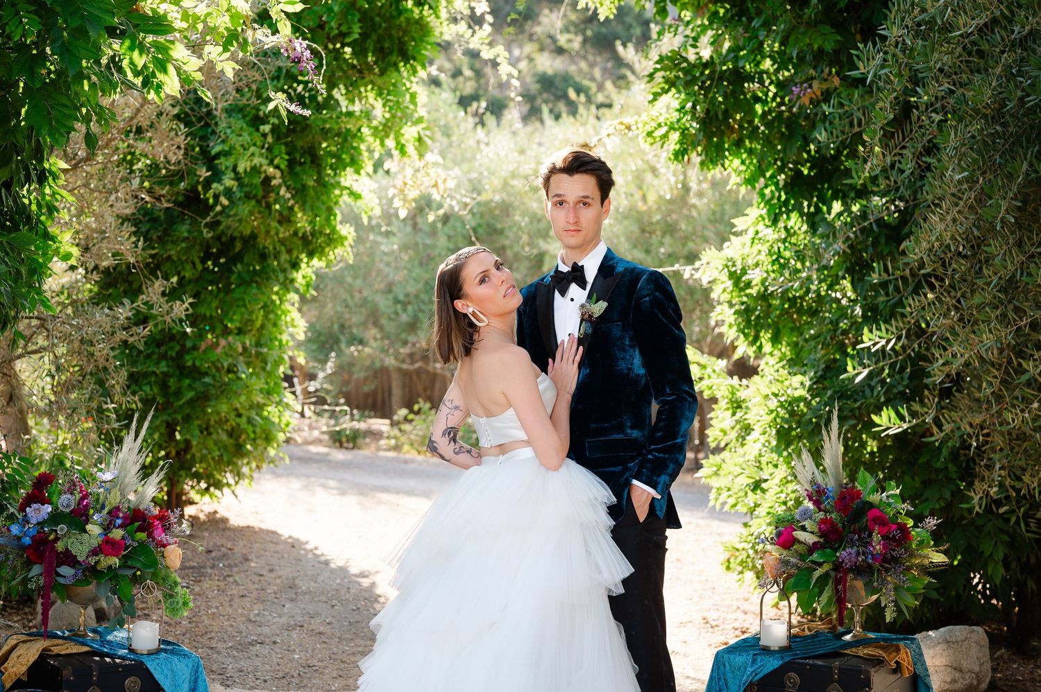 A couple stands together under a beautiful garden archway adorned with colorful floral arrangements.