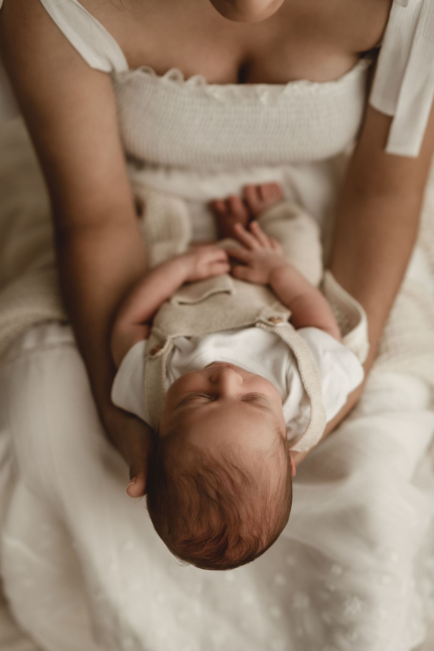 Overhead view of peaceful sleeping baby in white outfit resting on soft white fabric.