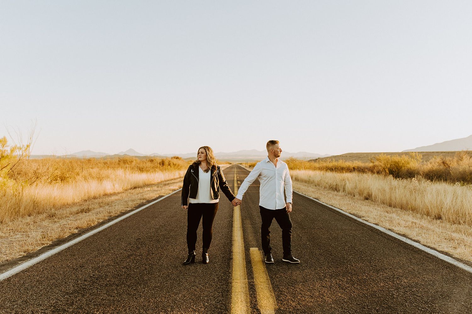 Couple stands together on empty rural road during golden hour.