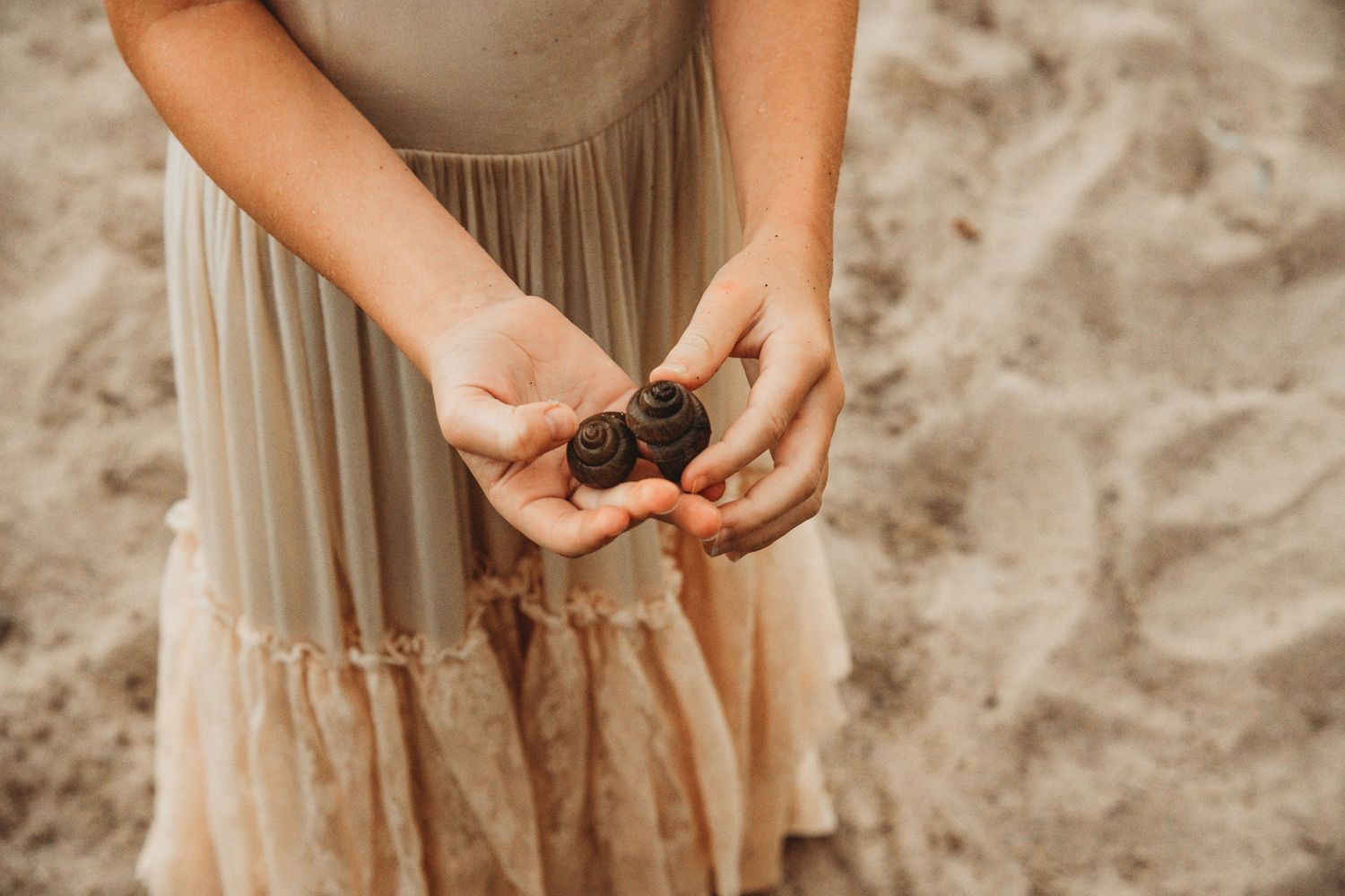 Hands gently hold small rocks on a sandy beach during a lifestyle photography session.