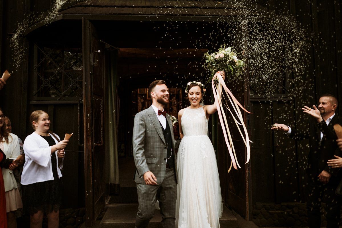 Joyful bride and groom exit church doors as guests shower them with rice confetti celebration.