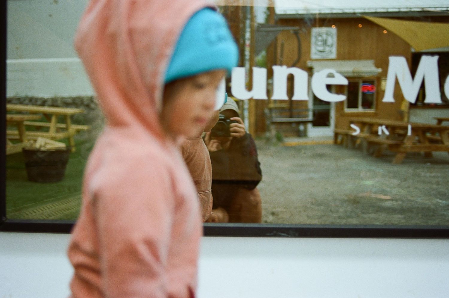 Person in pink hoodie walking past a blurred storefront.