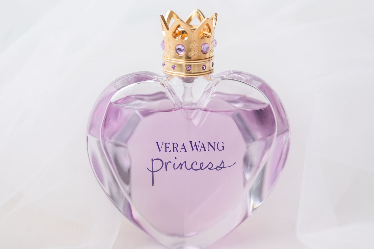 Purple heart-shaped Vera Wang Princess perfume bottle with gold crown cap on white background.