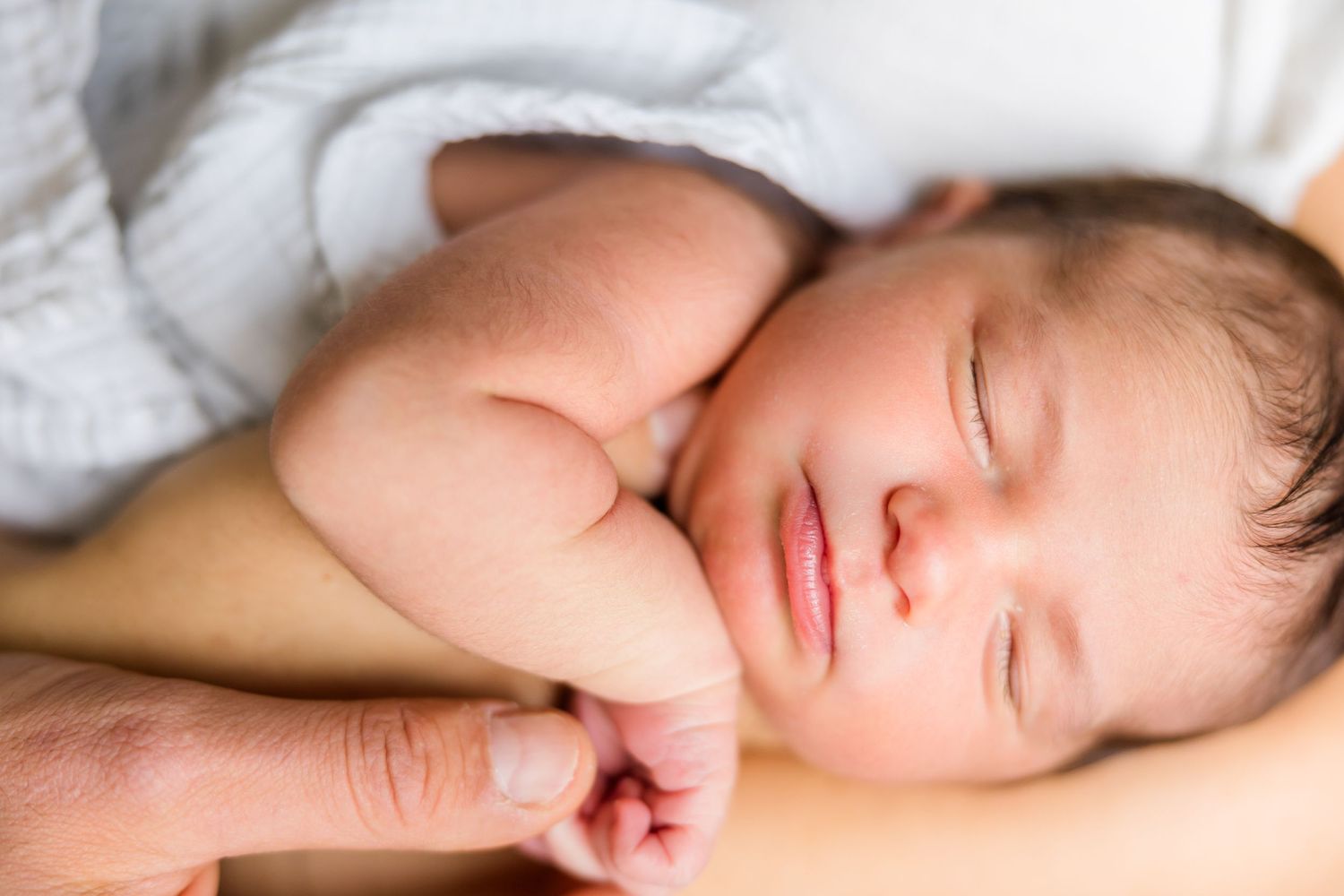 A peacefully sleeping baby nestled in soft white bedding with their hand curled near their face.