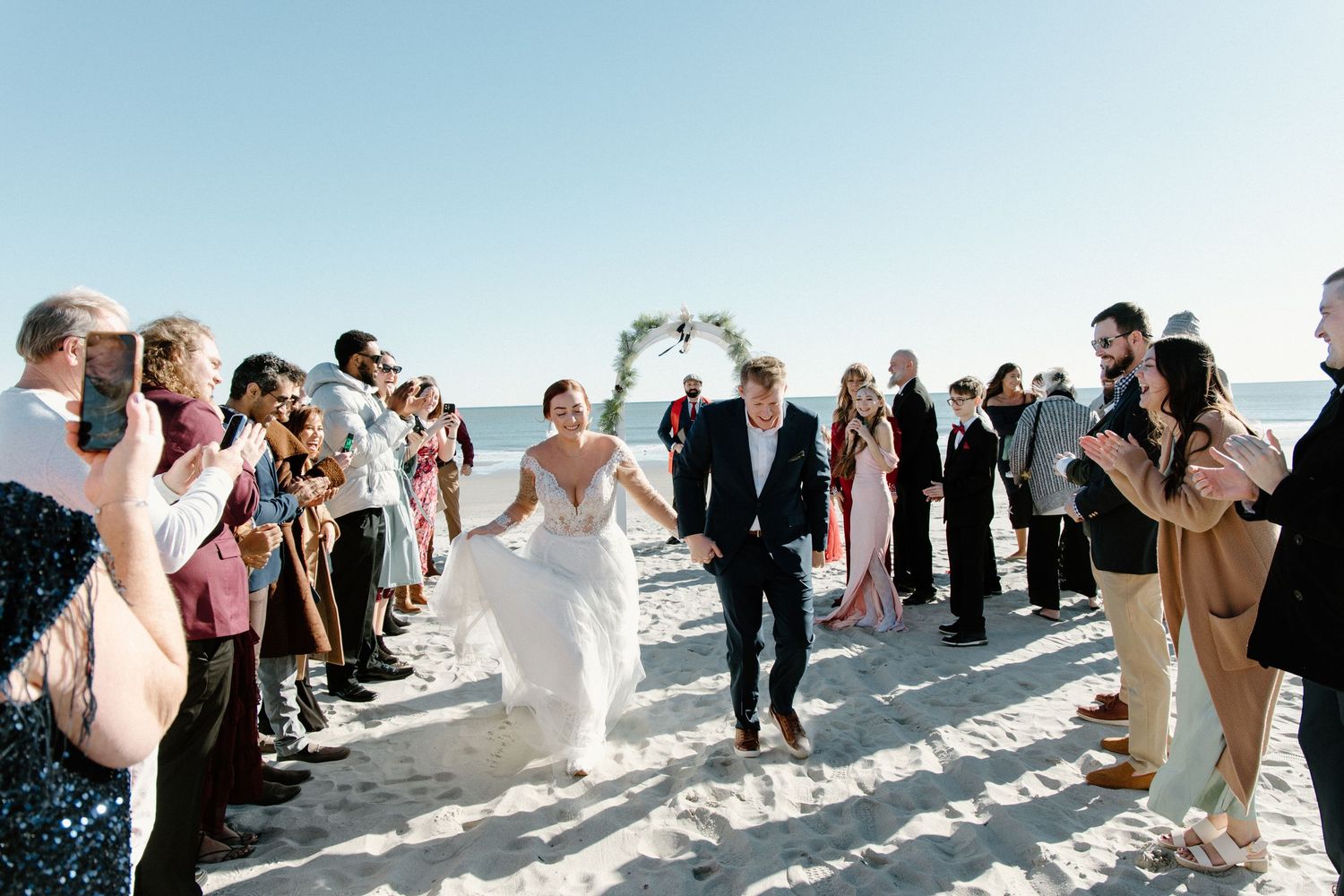 Wedding party creates a celebration pathway on white sandy beach as newlyweds run through during outdoor ceremony.