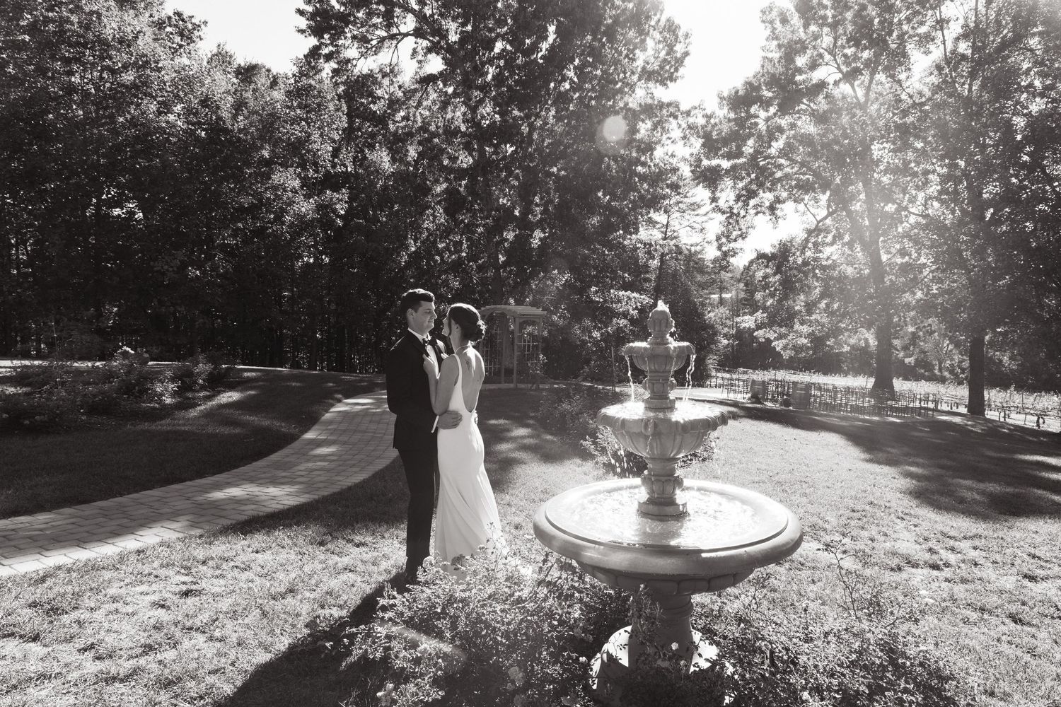 A romantic black and white wedding photo captures a couple standing by an ornate fountain in a scenic garden setting.