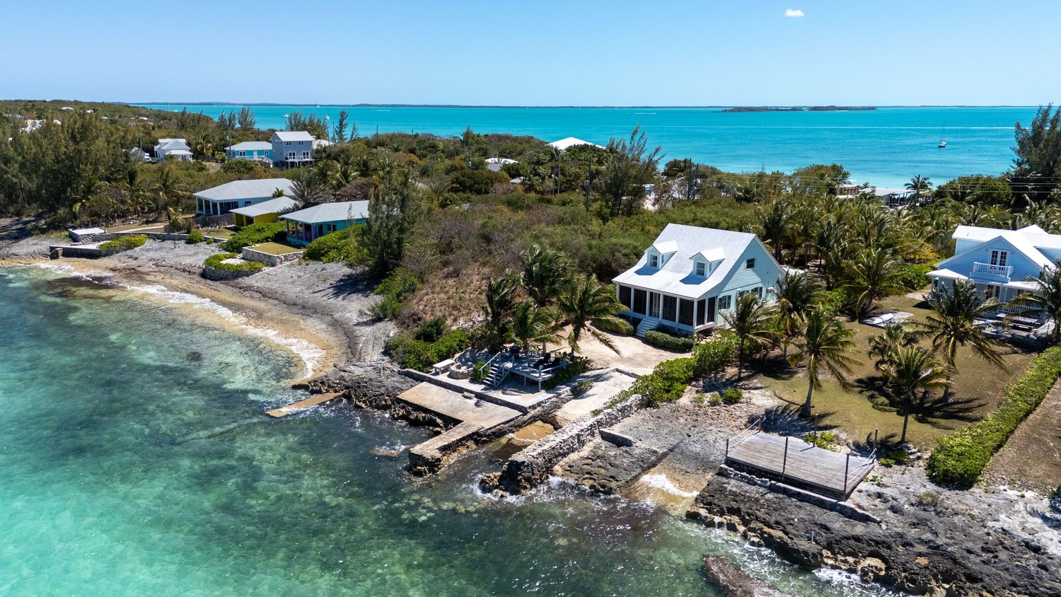Panoramic aerial view of luxury beachfront properties along a rocky coastline with crystal turquoise waters.