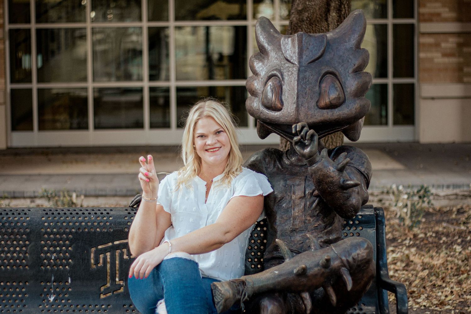 A student sits on a bench next to a bronze Sparky mascot statue on ASU campus.