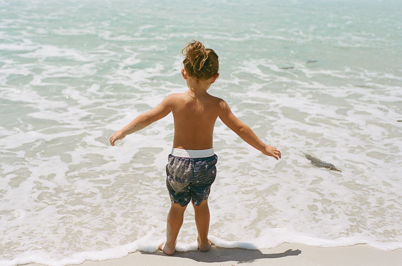 Child playing near the ocean waves on a sunny beach day.