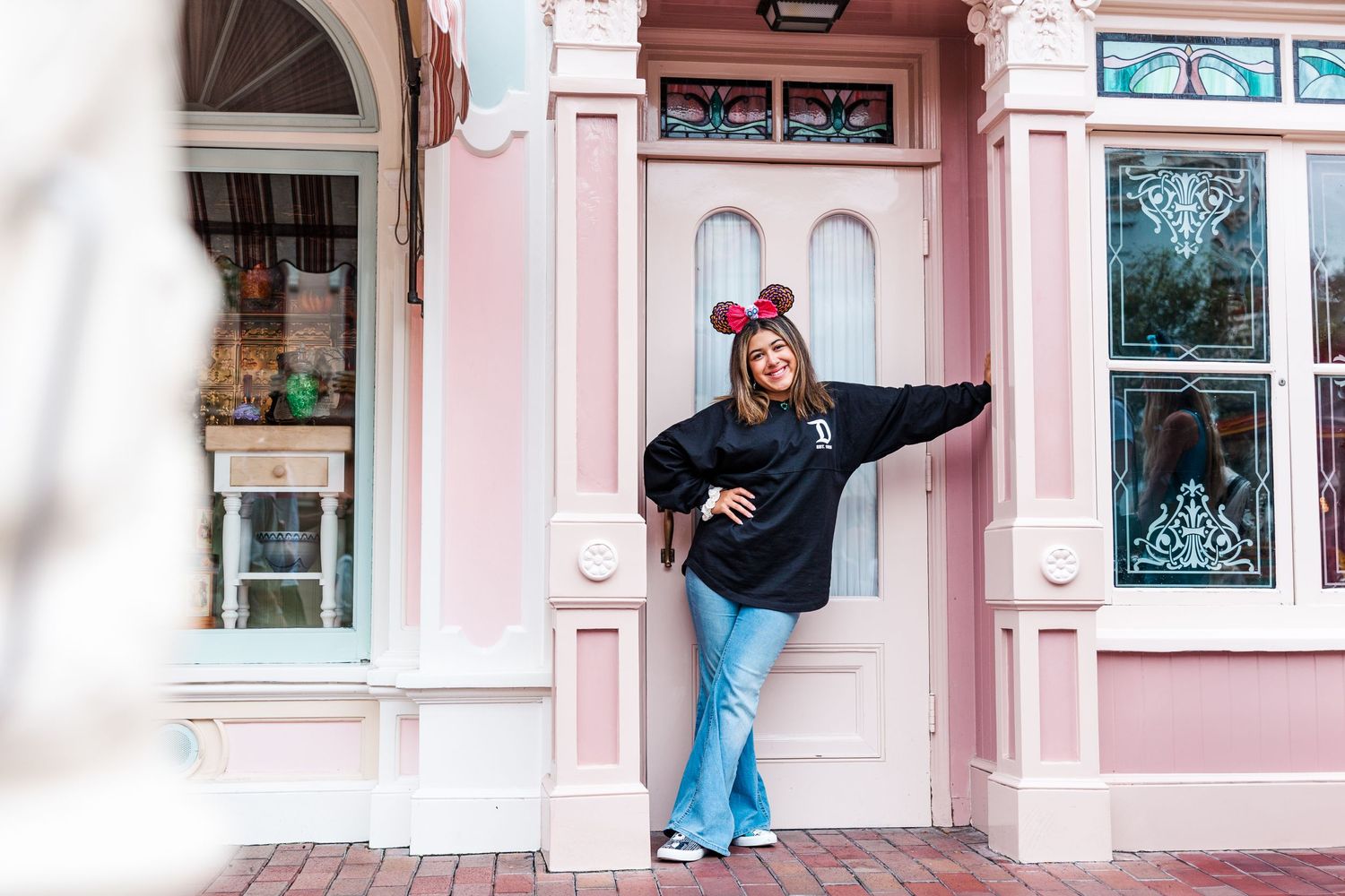 Playful pose against pink storefront wearing black sweater and jeans.