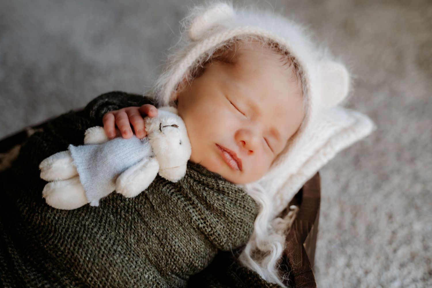 Sleeping newborn in knit outfit holds small stuffed toy while resting on blanket.