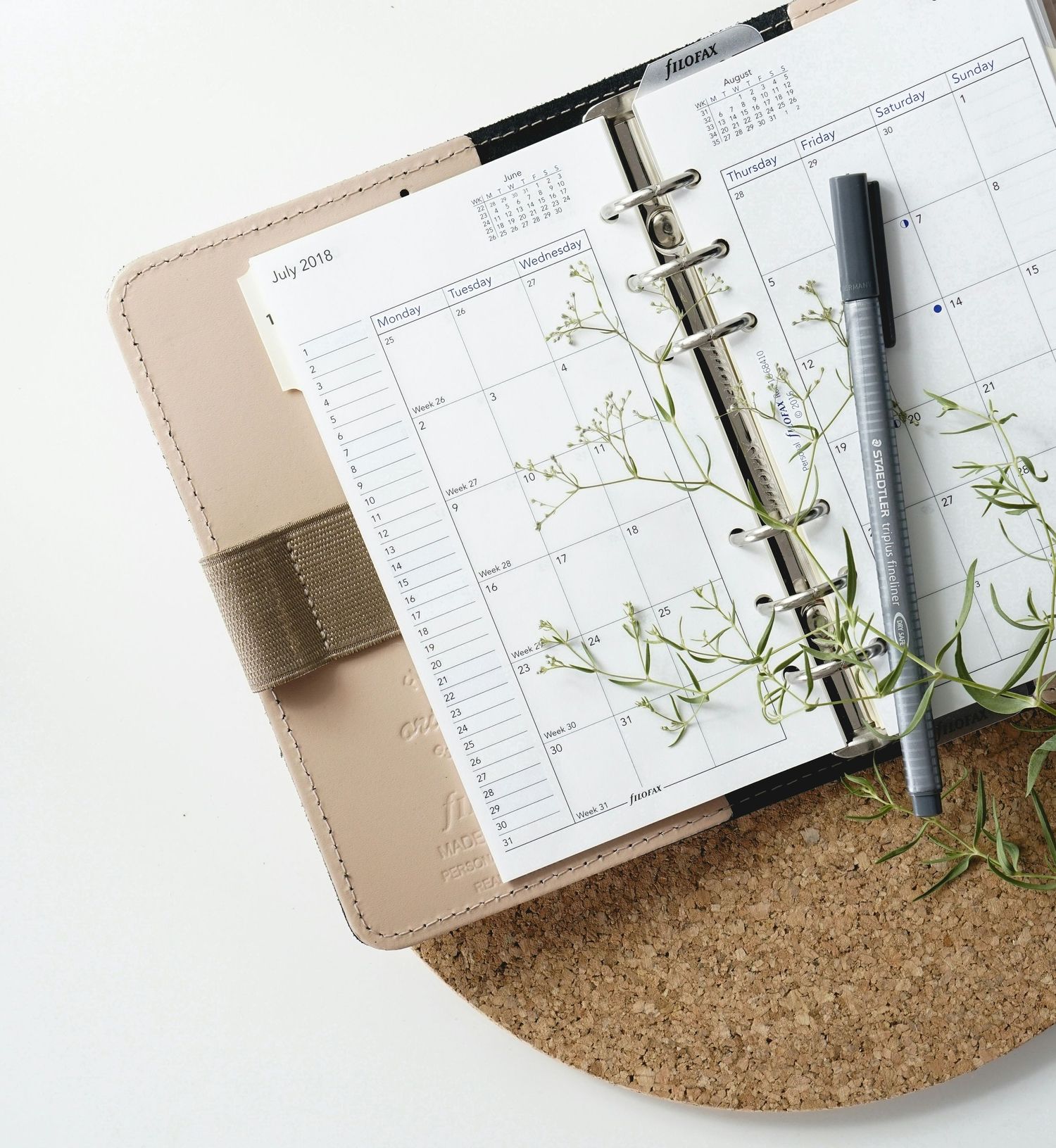 Open personal planner with floral design on pages and pen resting on cork surface background.
