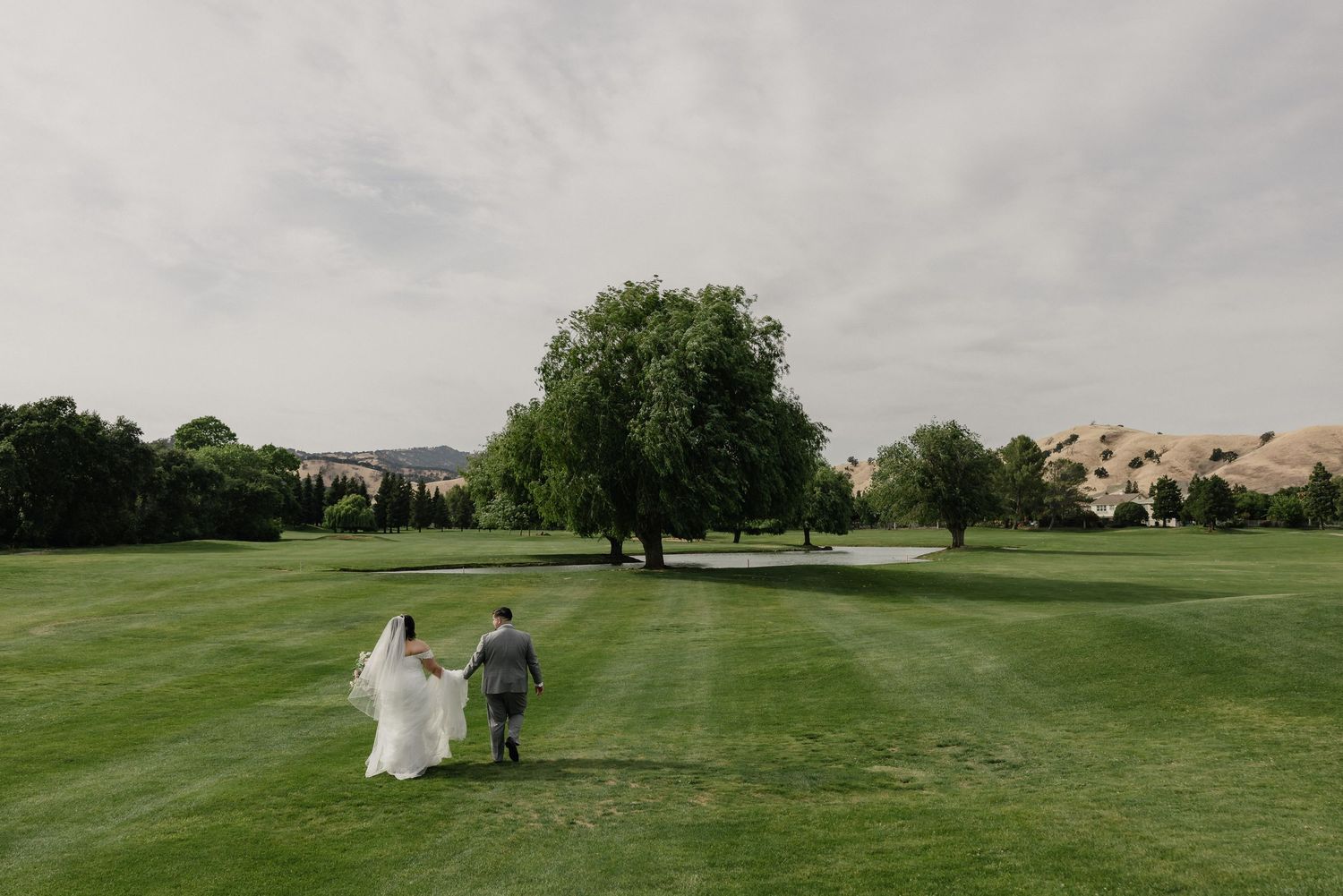 Wedding couple walk hand in hand across a lush golf course with rolling hills at the Top Knot Paradise Valley.
