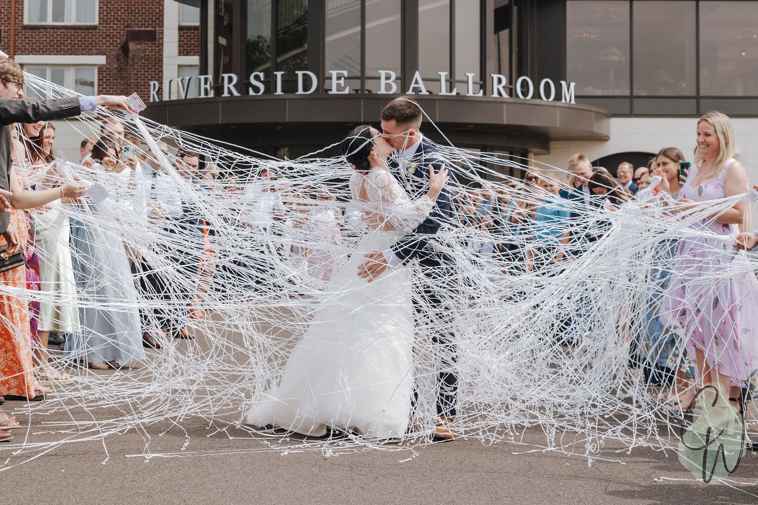 A group of partygoers dancing through a corridor filled with white streamers during a celebration event.