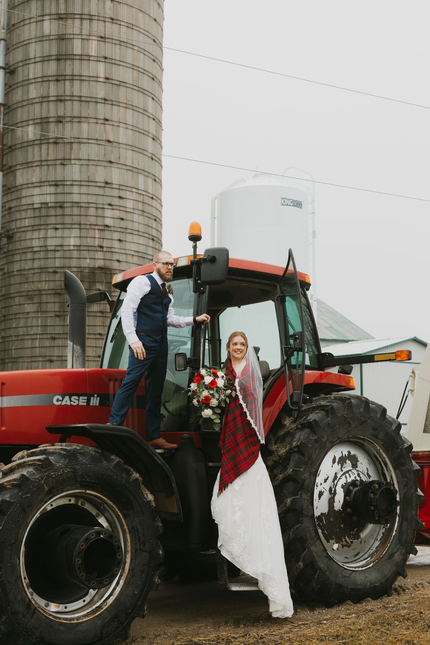 Wedding couple posing with red Case tractor near farm silo.