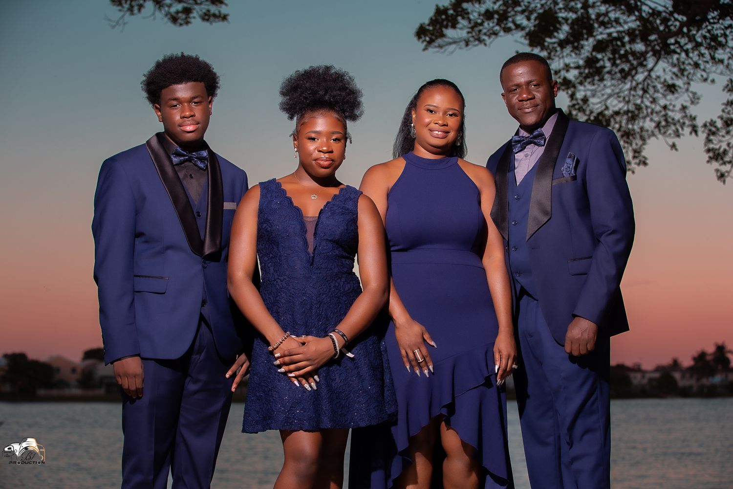 Four people in coordinating navy blue outfits pose together at sunset against a waterfront backdrop.
