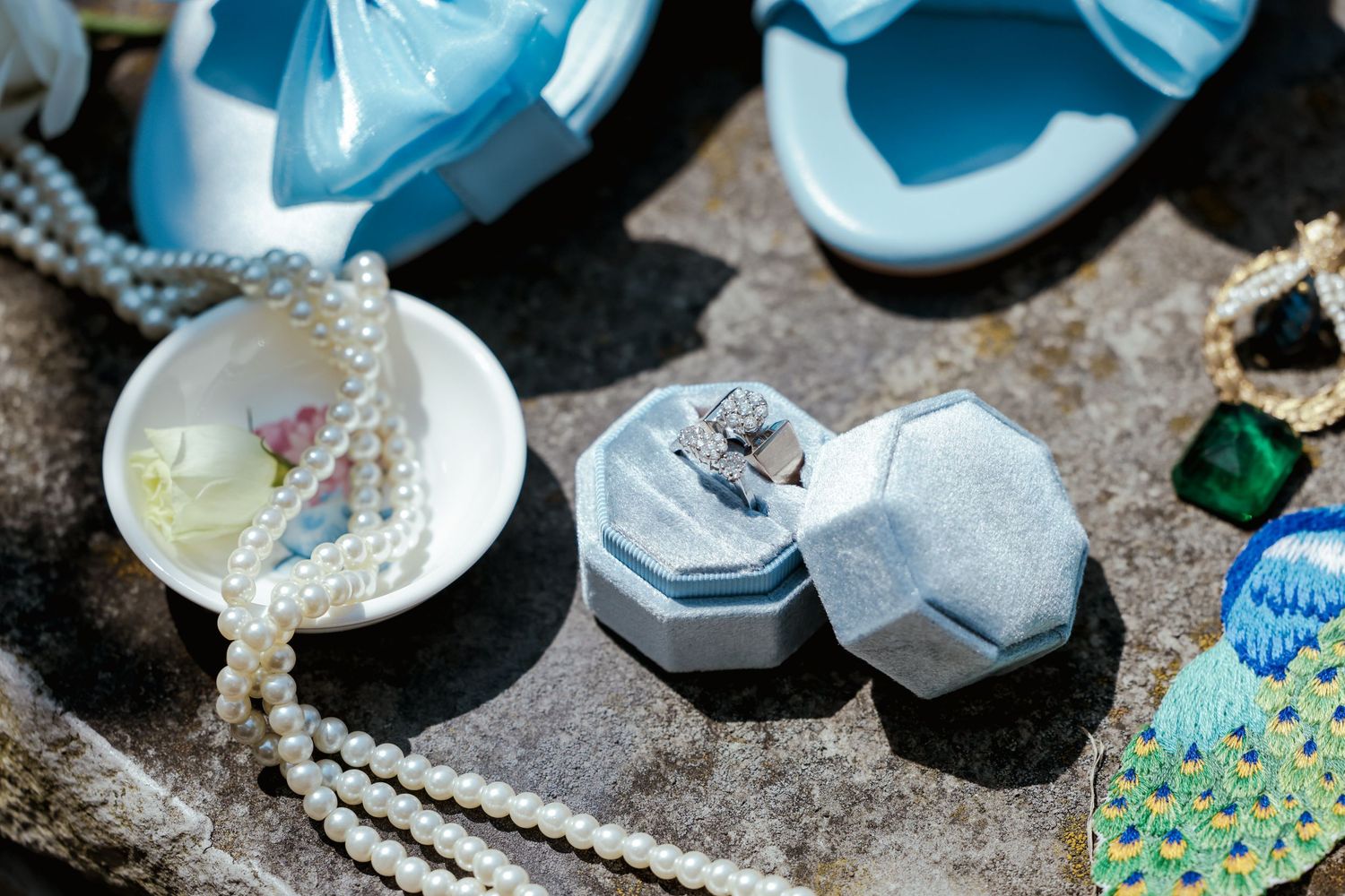 Wedding accessories including blue sneakers, pearl necklace, and jewelry boxes arranged on a textured surface.