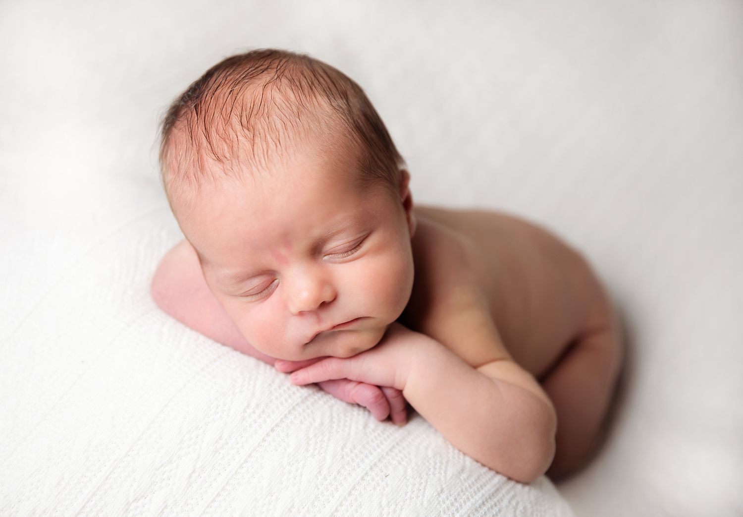 Sleeping newborn baby rests peacefully on soft white blanket during professional newborn photography session in Sidcup