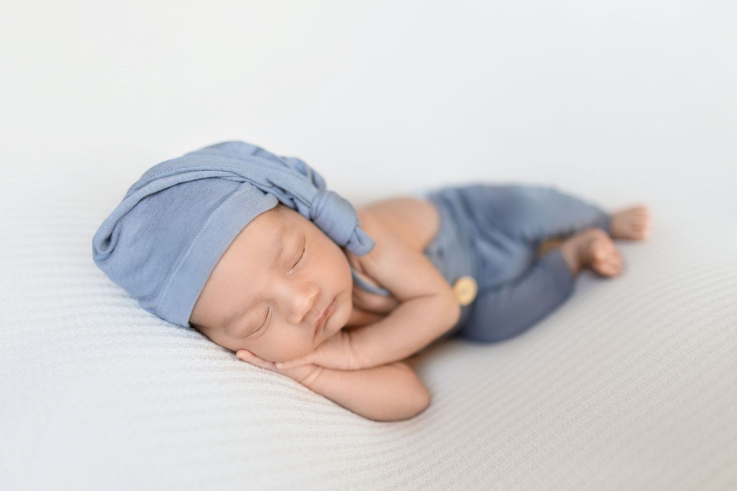 A sleeping baby in blue pajamas lying on a white surface shown from four different angles.