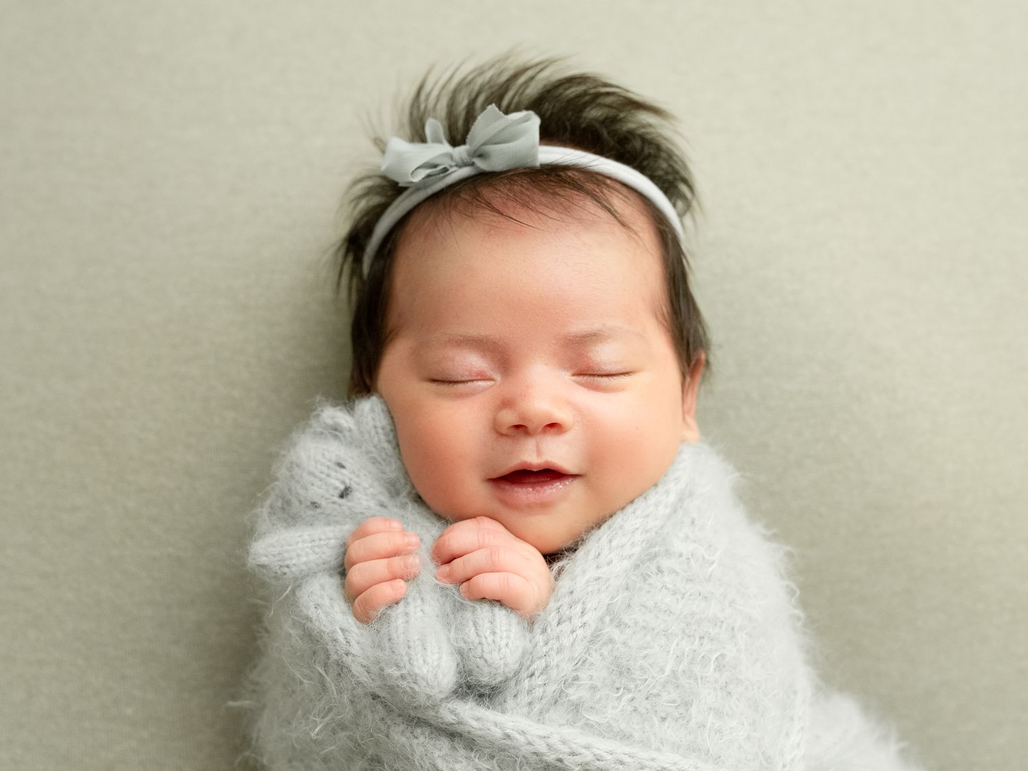 A sleeping newborn baby swaddled in soft white fabric against a neutral beige background.