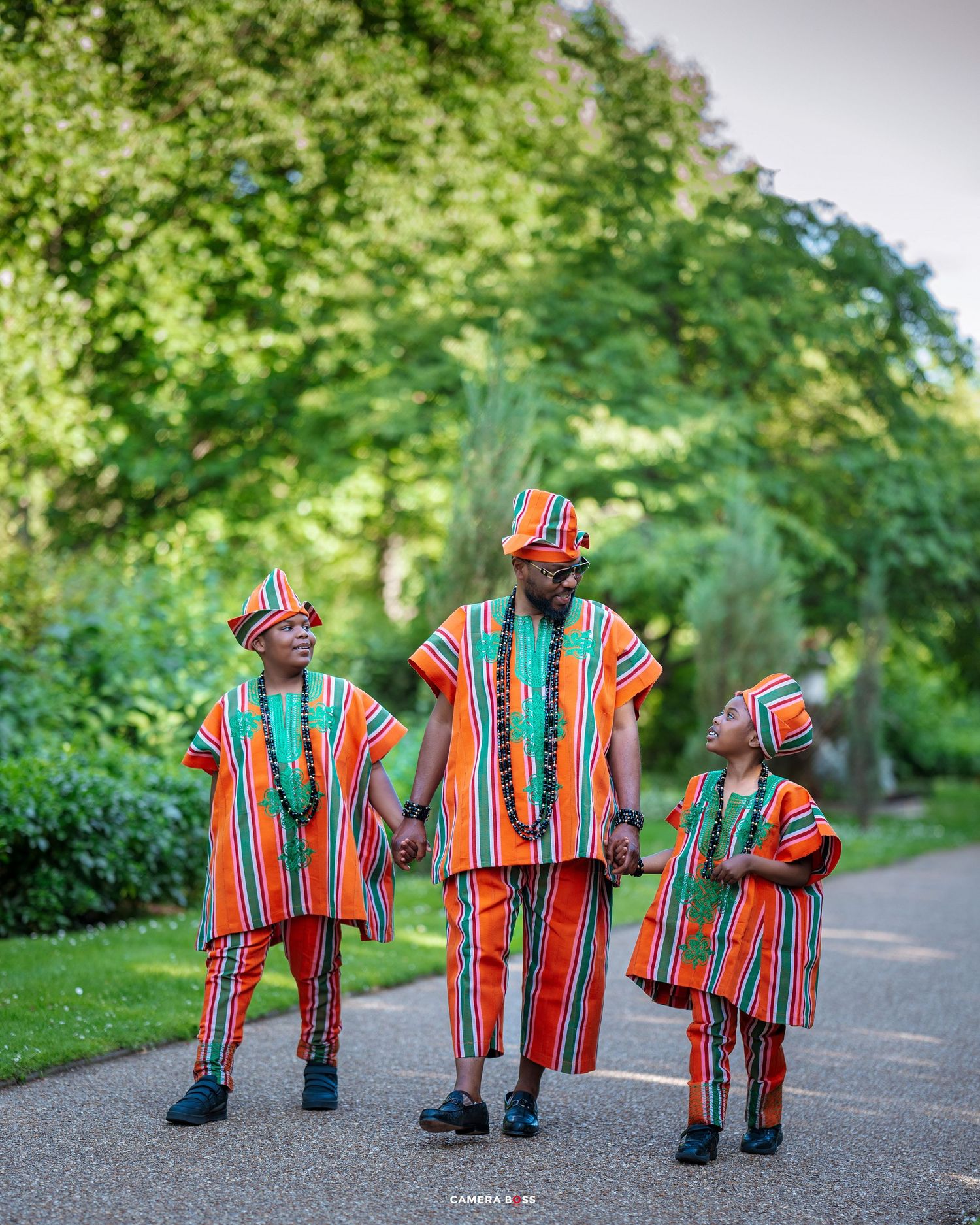 Colorful figures wearing vibrant striped outfits perform a synchronized walking sequence on a park pathway.