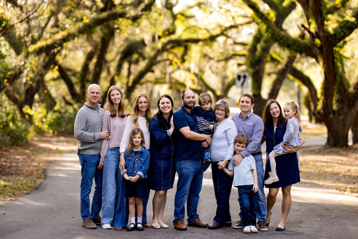 A group in coordinated blue and gray outfits poses together on a tree-lined path in warm autumn lighting.