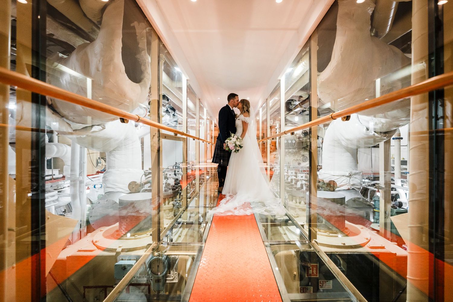 Wedding photo on Fingal hotel in the engine room.  Groom kissing bride full body landscape photo with engines in backdrop