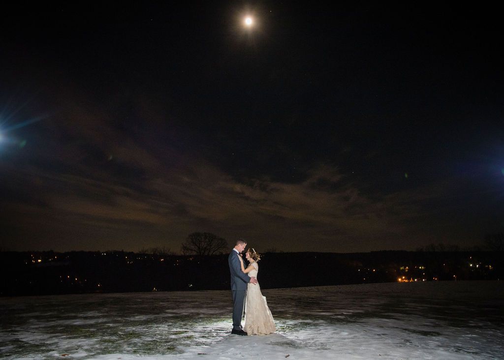 Newlyweds share an intimate moment outdoors with autumn foliage and rustic architecture in background.