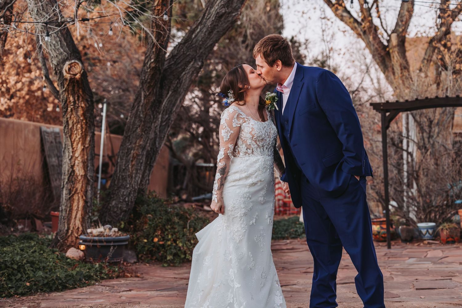 A couple in wedding attire dances together in a garden setting with autumn trees and rustic decor.