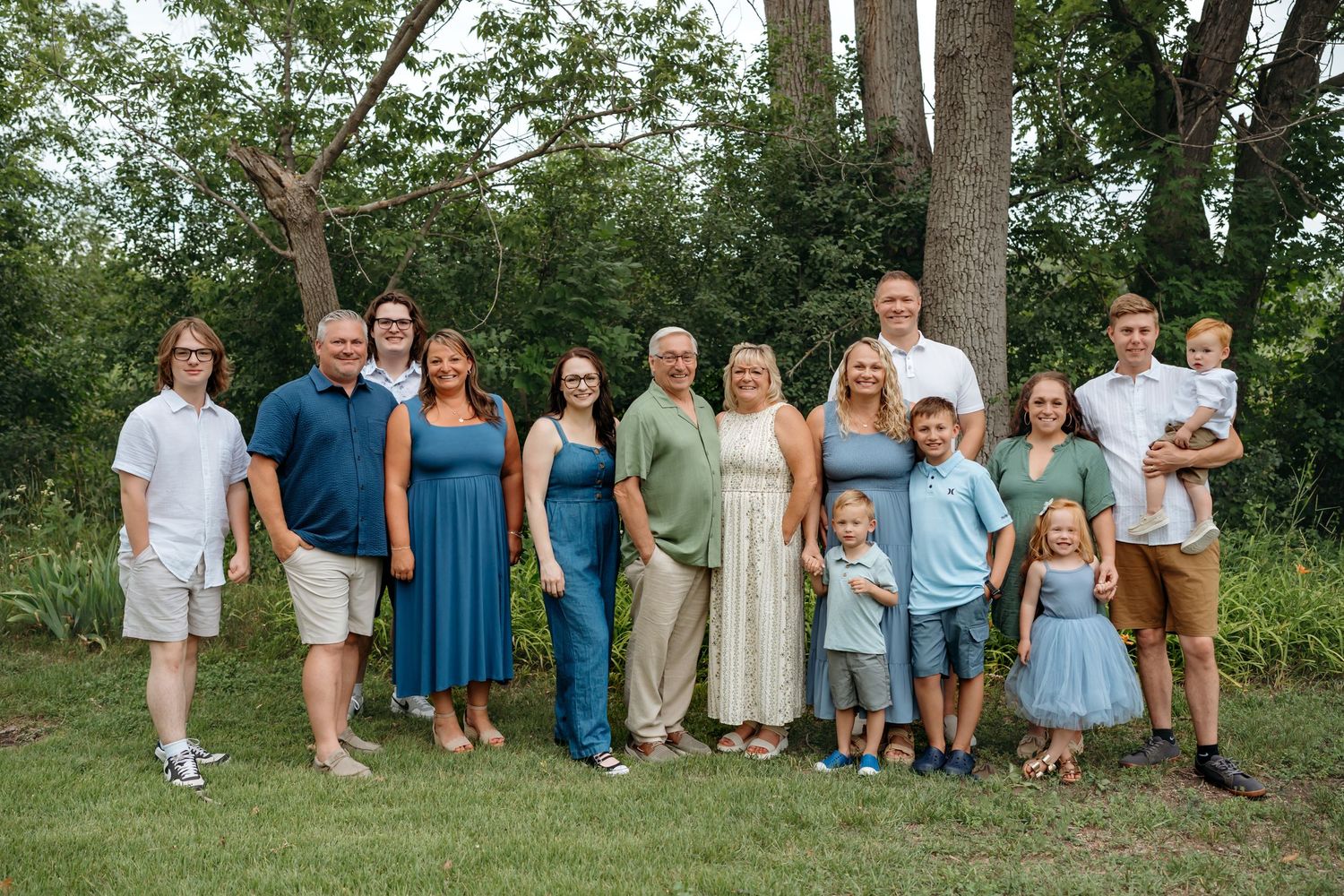 People dressed in coordinating blue and beige outfits pose together outdoors in front of trees.