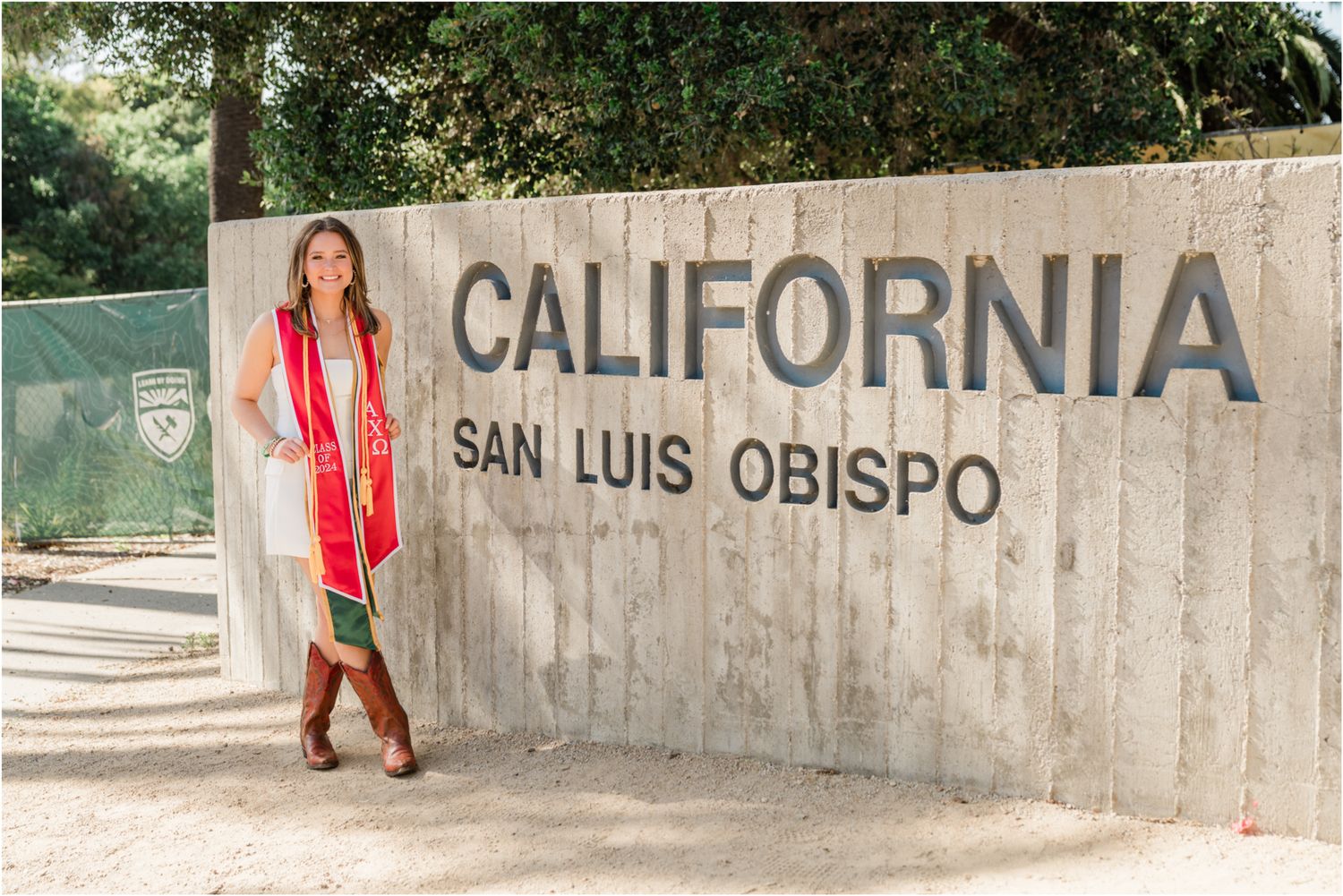 Cal Poly grad standing in front of Cal Poly sign wearing graduation stoles