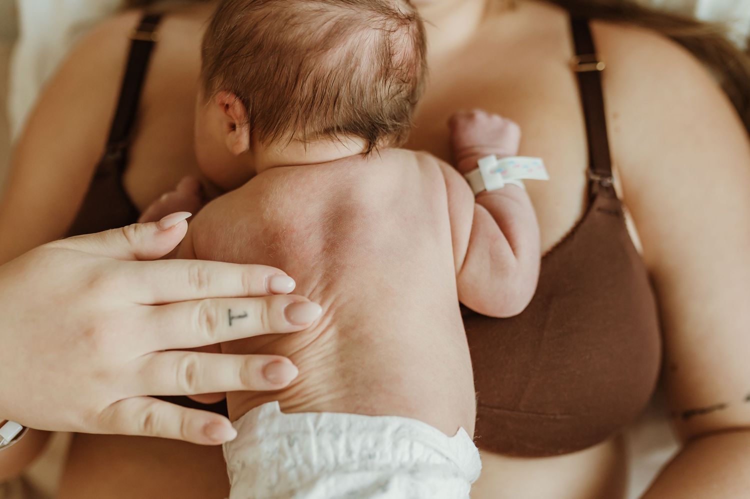 A parent's hand gently supports a baby wearing a diaper during a tender skin-to-skin bonding moment.