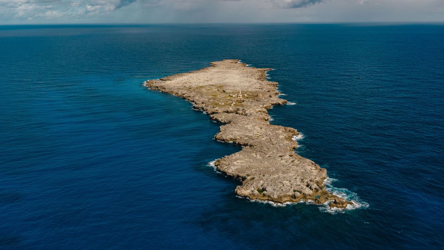 Panoramic aerial view of rocky coastline with turquoise Mediterranean waters and dramatic blue sky.