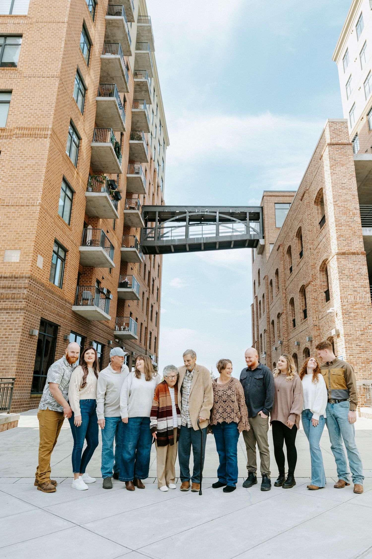 A group of people stand in a line against a brick building exterior with glass walkways overhead.