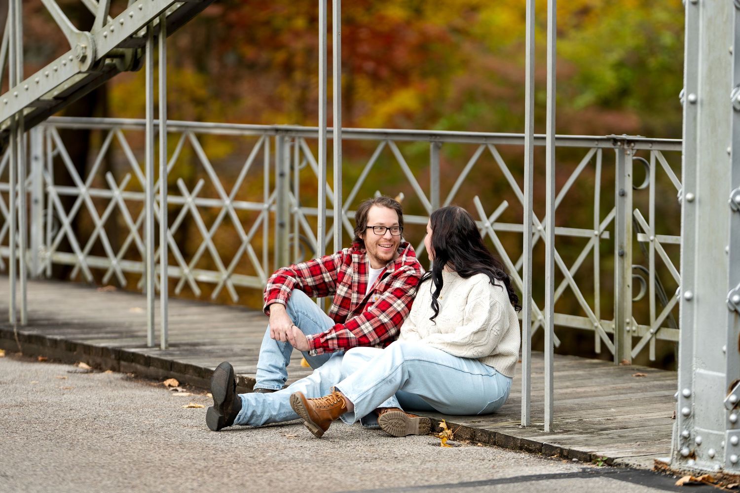Young couple sitting together on bridge floor surrounded by colorful autumn foliage background.